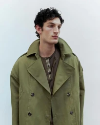 Model Aaron Shandel in an olive green trench coat against a plain white background for Antonioli Spring/Summer 2024