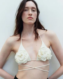 Model wearing a cream-colored floral appliqué halter bikini top against a plain white background for Antonioli