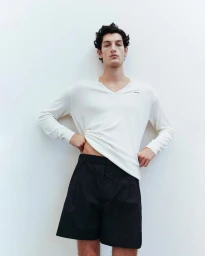 Male model wearing a white v-neck long sleeve top and black shorts against a white seamless background for Antonioli.