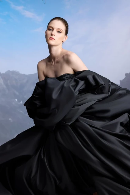 Fashion shot of a woman in a strapless black dress against a sky and mountain backdrop, portrait, posing, studio lighting.