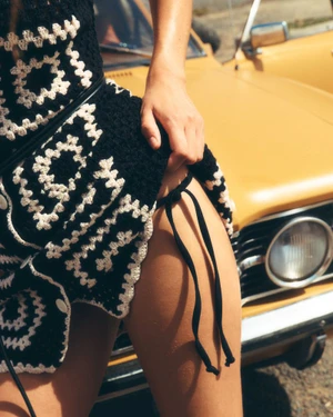 Close-up of a model wearing a black and white patterned knit dress standing in front of a yellow car.