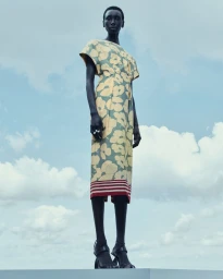 Model standing against a cloudy sky wearing a yellow and green floral print dress for Dries Van Noten High Summer 24 campaign.