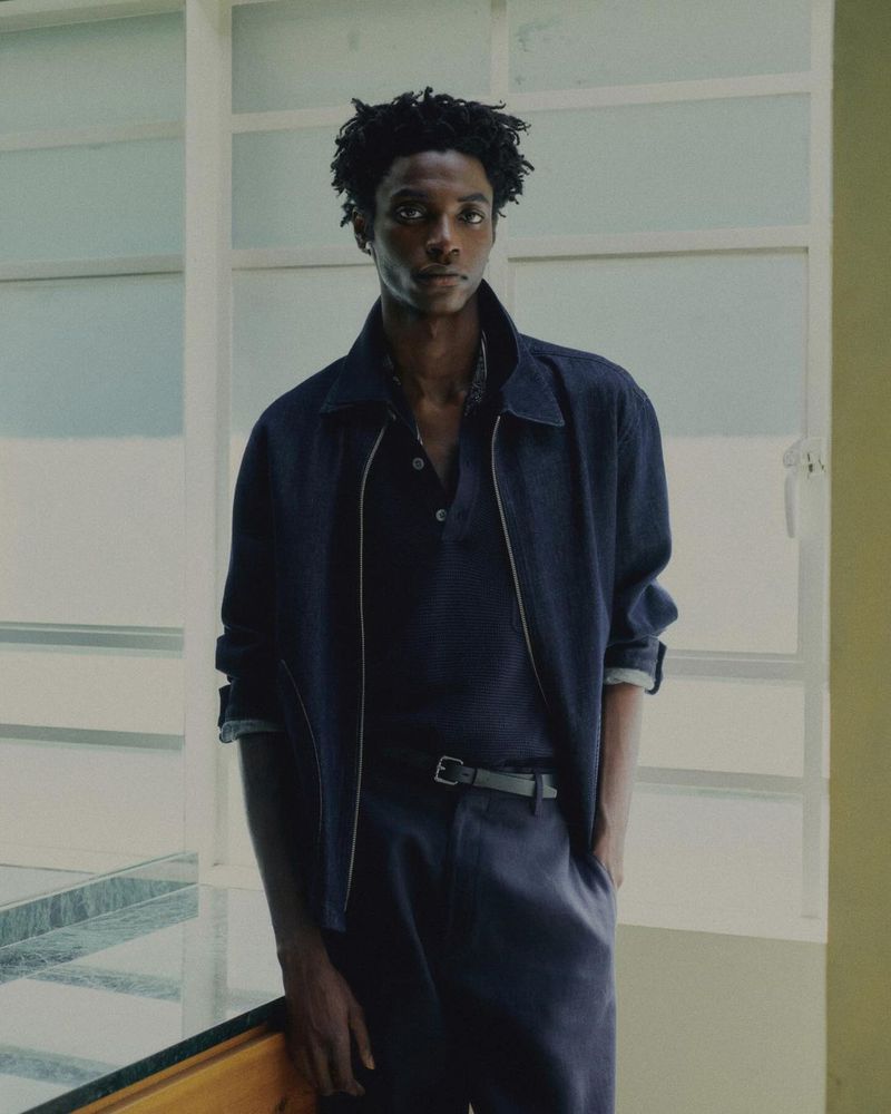 Adult male model in blue jacket and pants poses indoors against a window, shot in portrait orientation with soft, natural light.
