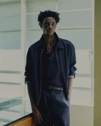 Portrait of a black man wearing a dark denim jacket and trousers in front of large paned windows for Massimo Dutti.