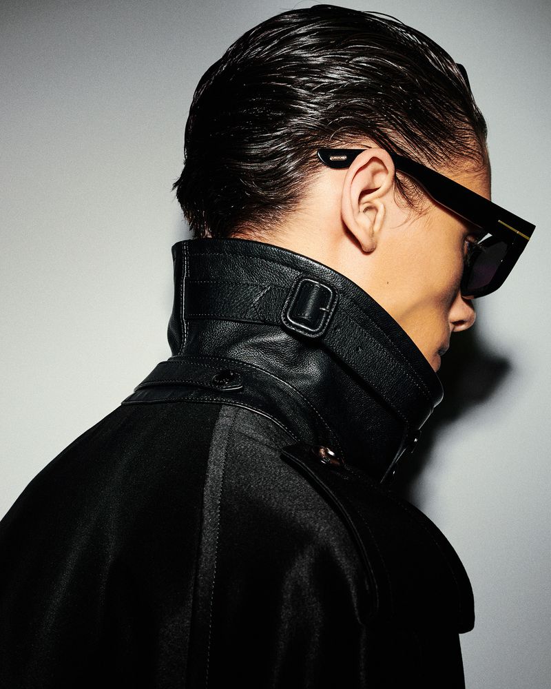 Elegant studio portrait of a man in a black coat and sunglasses. Close-up shot with wet hair, stylish look, and neutral background.
