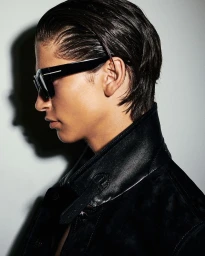 Profile portrait of a male model wearing dark sunglasses and a black leather jacket against a white wall.
