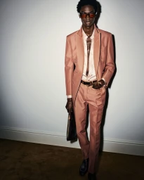 Model wearing a pink suit holding a bag against a plain wall for Tom Ford Menswear Spring Summer 24 collection campaign.