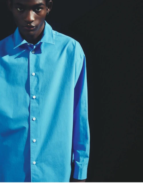 Portrait of a black male model in a light-blue dress shirt against a dark background, showcasing the shirt's design and color.
