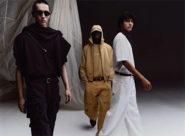 Three male models wearing dark, yellow, and white outfits in front of a textured fabric backdrop for Zara Basez.
