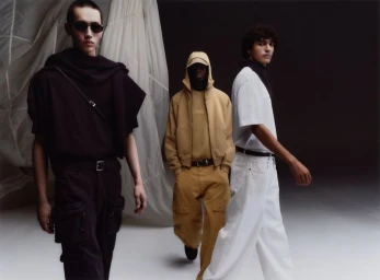 Three male models wearing dark, yellow, and white outfits in front of a textured fabric backdrop for Zara Basez.
