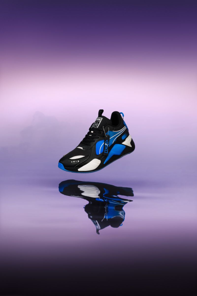Black and blue Puma sneaker, in a studio product shot with a violet to white gradient background, reflected in a glossy surface.