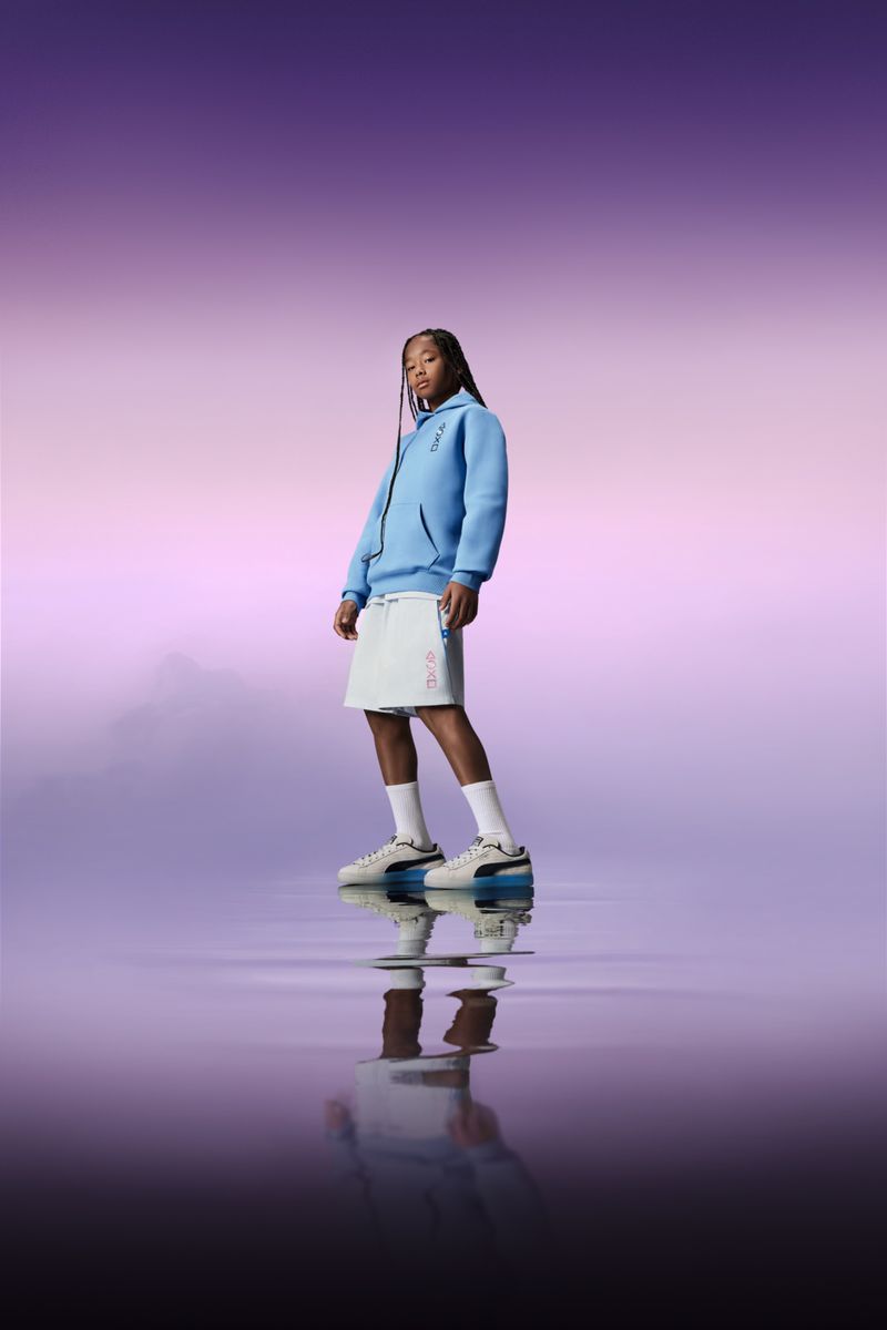 A person standing with their reflection in a watery-looking environment under a pastel gradient sky, wearing a hoodie and sneakers.