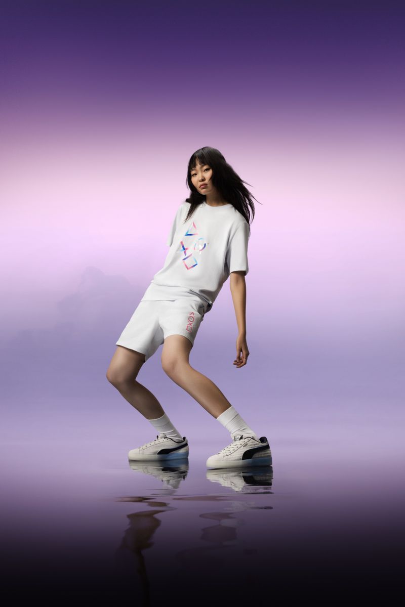 Athletic woman in white t-shirt and shorts strikes a pose wearing Puma sneakers against a purple and reflective backdrop.