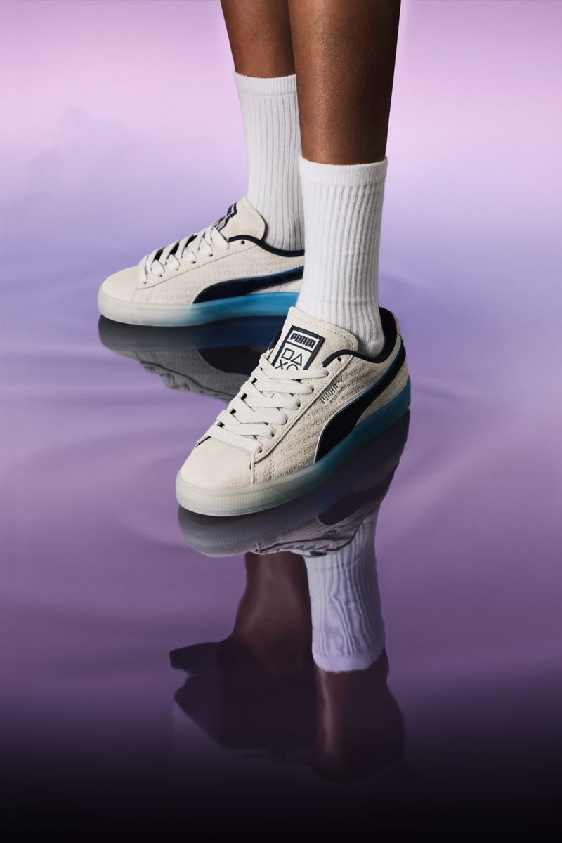 Close-up of white and black Puma sneakers with white socks on a person's legs against a mottled purple background, product shot.