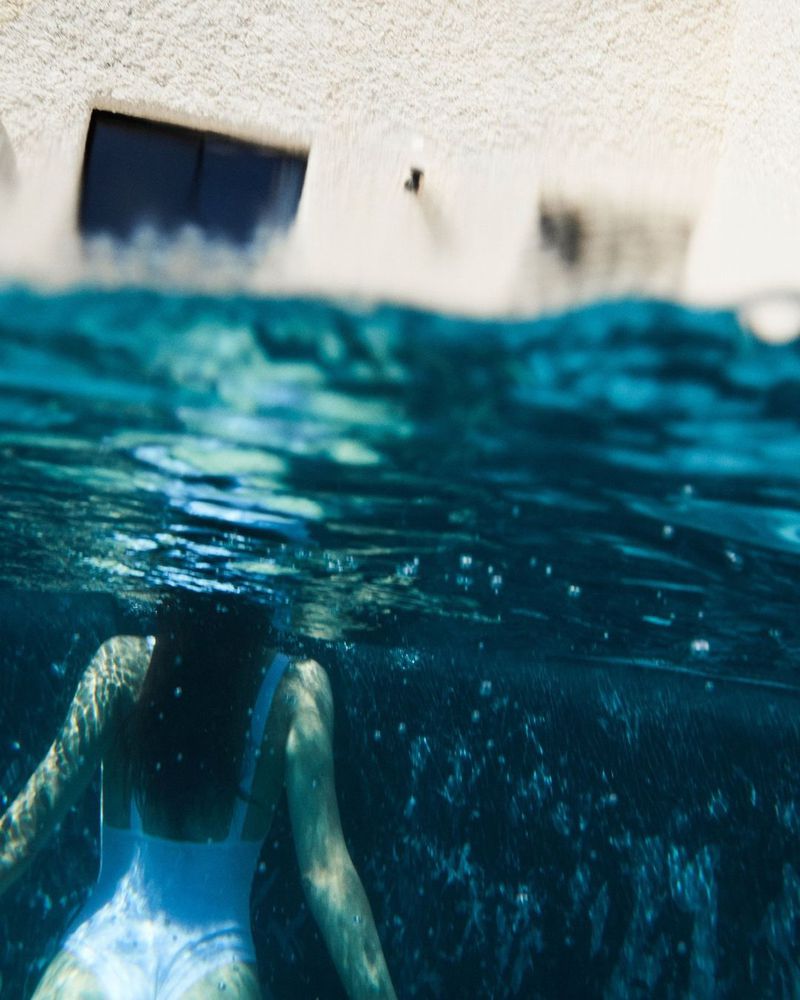 Underwater view of a woman in a white bathing suit swimming in turquoise water, with a white building partially visible above.