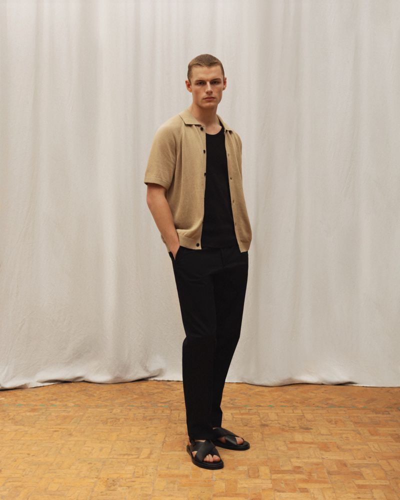 Full-length shot of a young adult male in a casual outfit of cardigan, t-shirt, and trousers, posing in front of a white curtain.