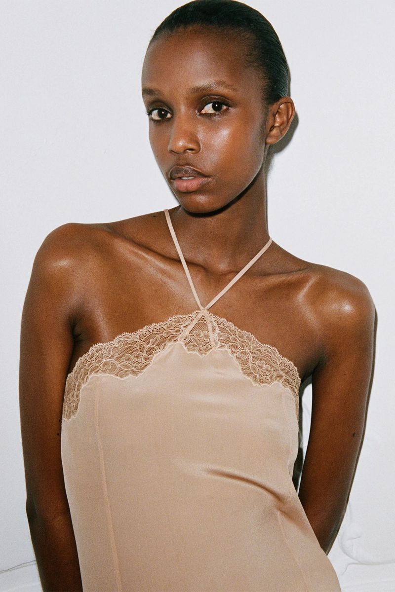 Close-up studio shot of an adult woman wearing a lace-trimmed beige halter dress against a light background.