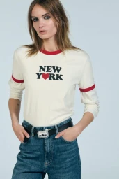 Model wearing a white ringer t-shirt with red trim and New York text, paired with blue jeans and a black belt against a grey background.