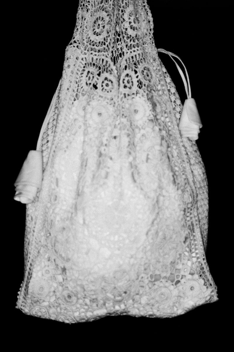 Elegant white lace bag with drawstring closure and decorative tassels, set against a stark black background, emphasizing its intricate design.