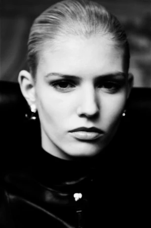 Close-up portrait of an adult female with slicked-back blonde hair wearing a black top in a studio setting with neutral facial expression.