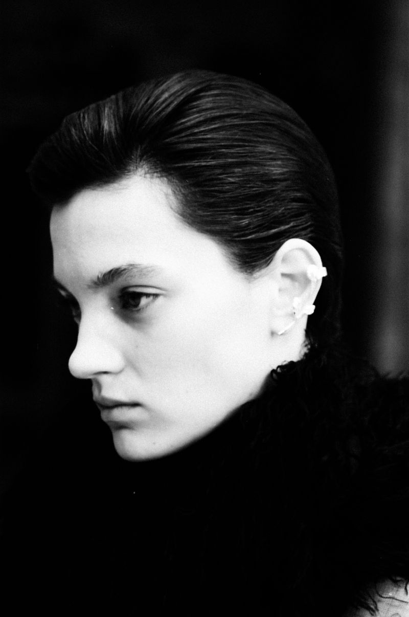 Black and white portrait of a young adult woman in profile, facing left, with dark hair and a white ornamental earring.