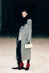 Model in a grey coat and black scarf holding a white handbag for Magda Butrym
