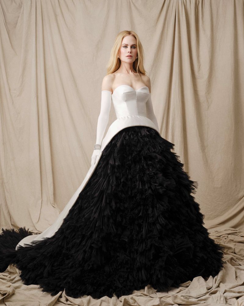 Nicole Kidman stands wearing an elegant white and black gown with matching gloves in a posed photo studio fashion shot. 