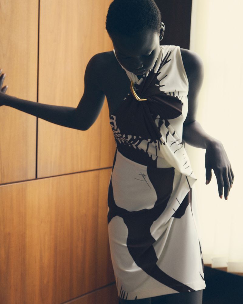 Elegant Black woman in a printed sleeveless dress poses next to a paneled wall, offering a look of poised fashion.