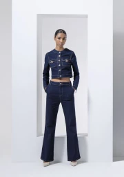 Model wearing a dark denim cropped jacket and matching flare jeans standing within a white geometric frame in a studio.