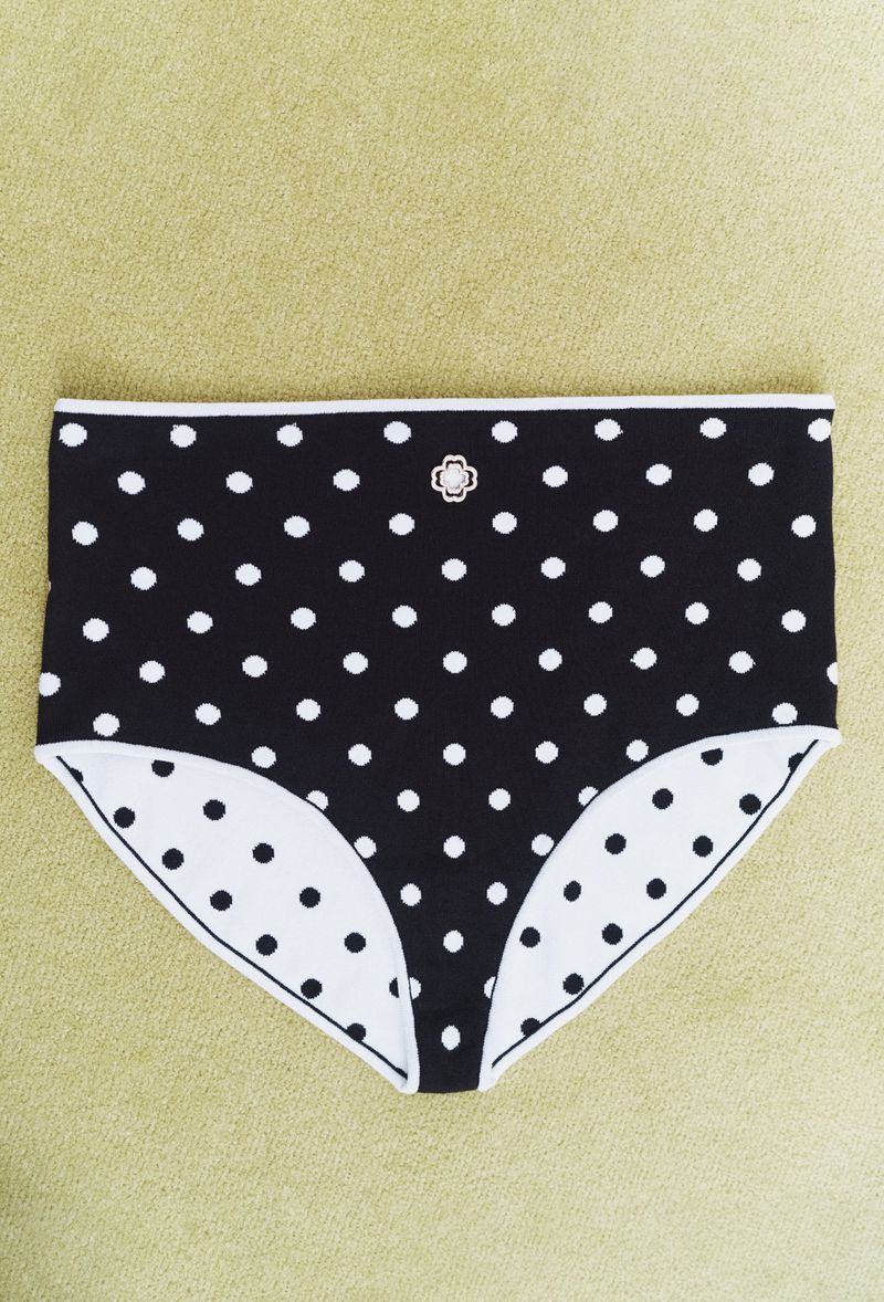 Black and white polka dot high-waisted underwear with a small decorative embellishment, set on a plain, light green surface.