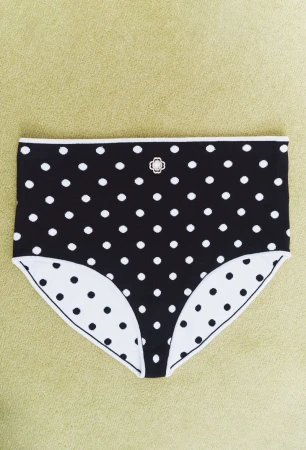 Black and white polka dot high-waisted underwear with a small decorative embellishment, set on a plain, light green surface.
