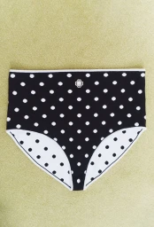 Black high-waisted polka dot briefs with white trim and a small logo laid flat on a light olive textured fabric surface.