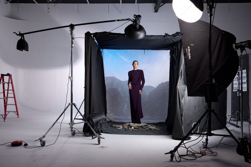 Fashion shoot in a photo studio featuring an adult female model in a long purple dress in front of a mountain backdrop.