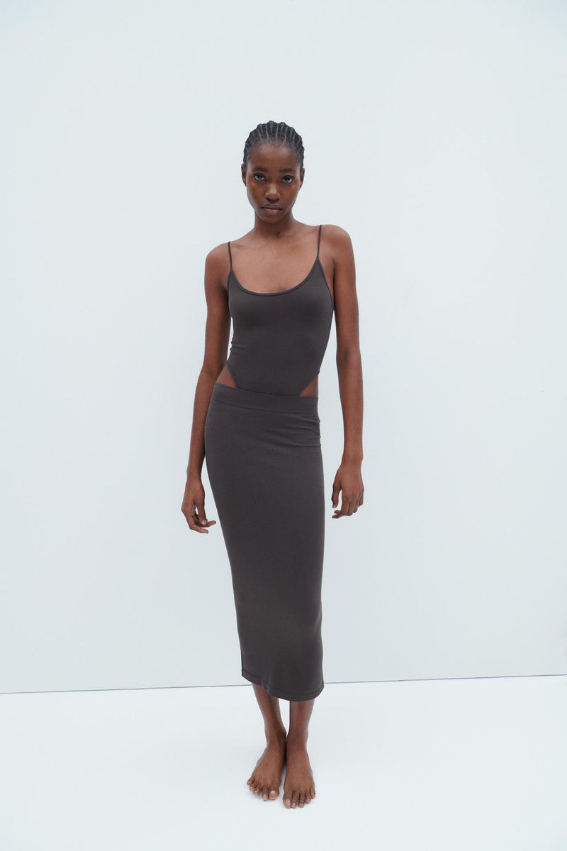 Woman in a grey dress with cutouts poses in a neutral setting showcasing fashion and style for a contemporary look.