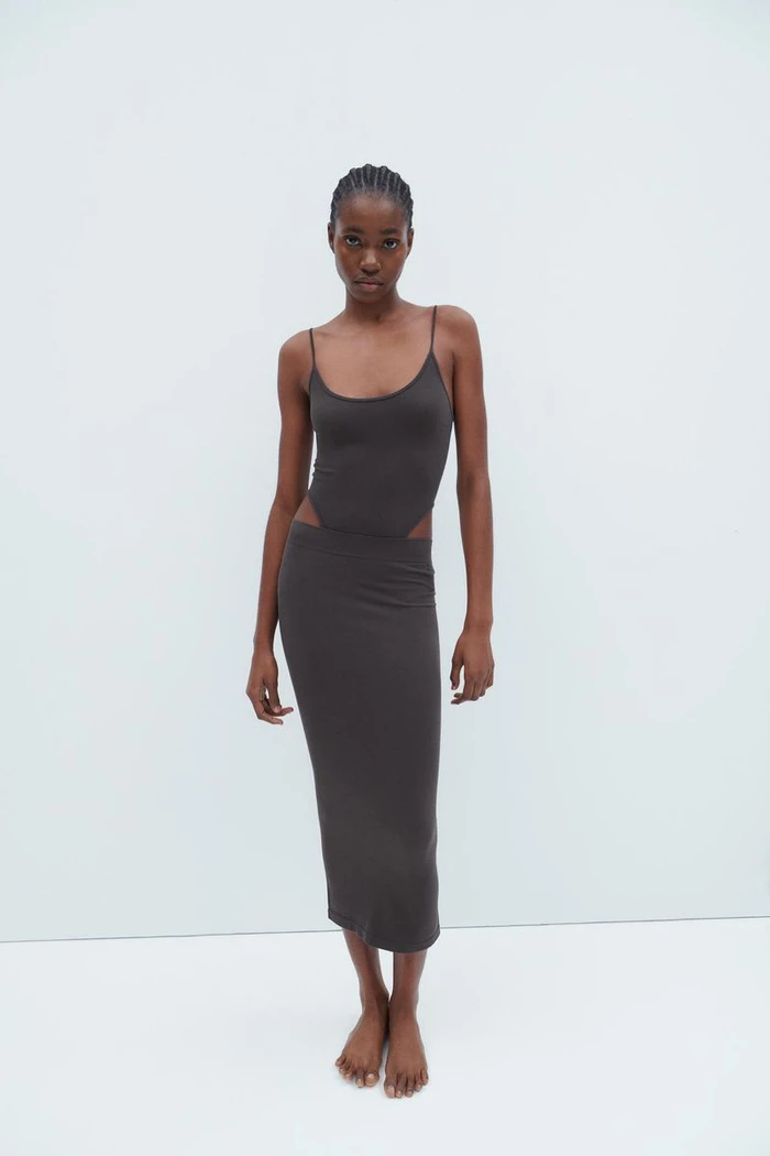 Model wearing a dark grey cutout midi dress standing against a plain white seamless studio background.