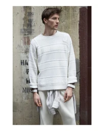 Model Finnlay Davis wearing a cream textured knit sweater and matching trousers against a weathered concrete wall.