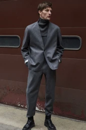 Model Finnlay Davis wearing a grey suit and dark turtleneck against a red door for Rag and Bone