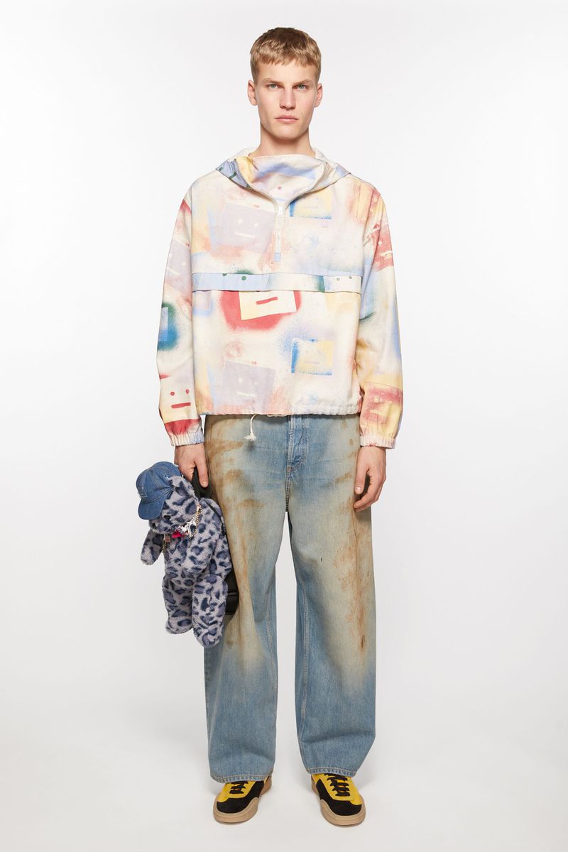 Full-length studio shot of a young adult male fashion model wearing an abstract-patterned jacket and baggy jeans, holding a stuffed animal.