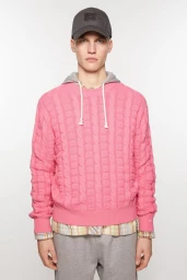 Model wearing a pink cable knit sweater over a plaid shirt and grey cap for Acne Studios S/S 24