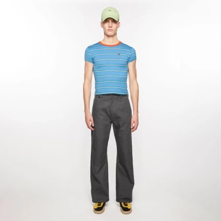 Male model wearing a fitted blue striped t-shirt, charcoal wide-leg trousers, and a pale green cap against a white background.