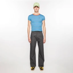Male model wearing a fitted blue striped t-shirt, charcoal wide-leg trousers, and a pale green cap against a white background.