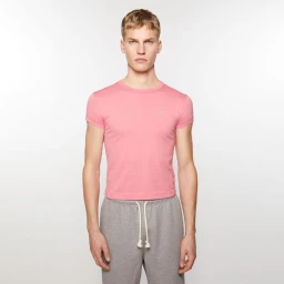 A male model wearing a fitted pink short-sleeve t-shirt and grey sweatpants against a plain white studio backdrop.