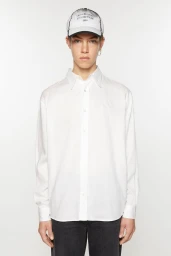Model wearing a white button-down shirt, dark trousers, and a branded baseball cap against a plain white background.