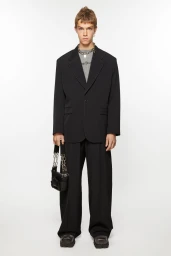 Male model in a black suit holding a small handbag against a solid white background
