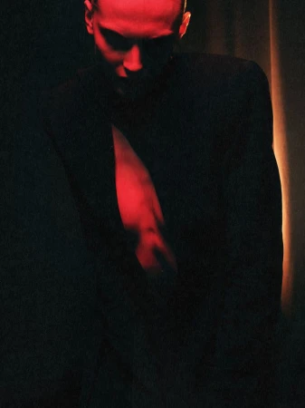 Model wearing an open structured black blazer illuminated by dramatic red light against a dark background.