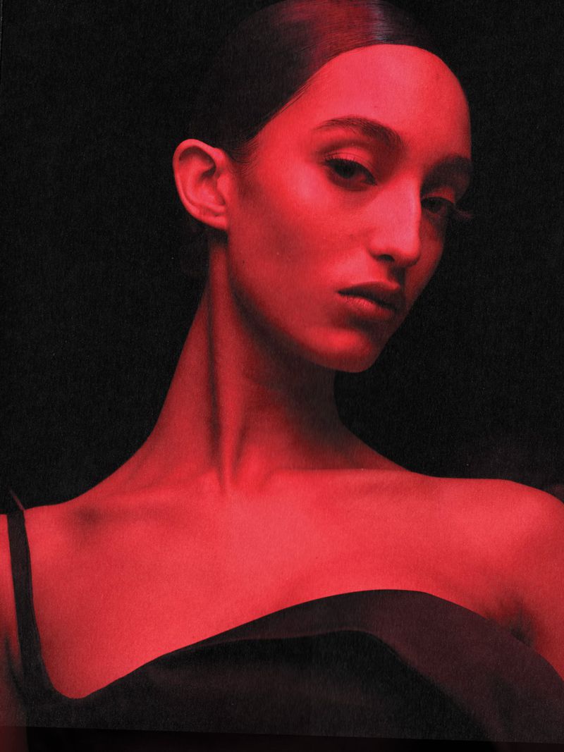 Headshot of a young adult female model bathed in red light against a dark backdrop, highlighting her facial features and sleek hairstyle.