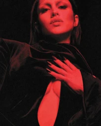 Model Amelia Gray illuminated in dramatic red light wearing a draped black velvet cutout garment against a dark backdrop for Mugler.