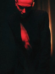 Model wearing an open structured black blazer illuminated by dramatic red light against a dark background.