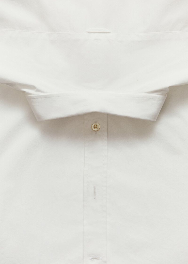 Close-up of a white dress shirt with a visible button and collar, showcasing texture and garment construction.