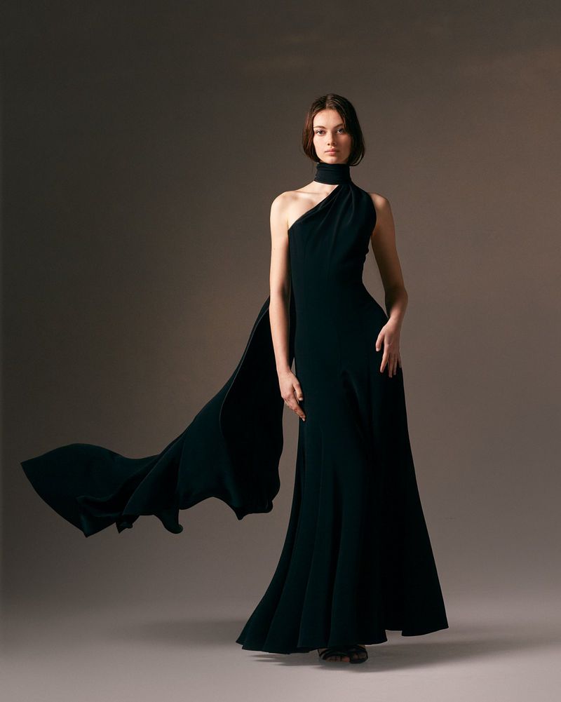 Woman in a black one-shoulder gown with flowing fabric, posing in a studio. Elegant formal wear fashion photography.